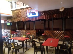 A restaurant with red tables and black chairs, wooden paneling on the walls, and a television mounted on the wall. - Jostem Inn (Ruiru)