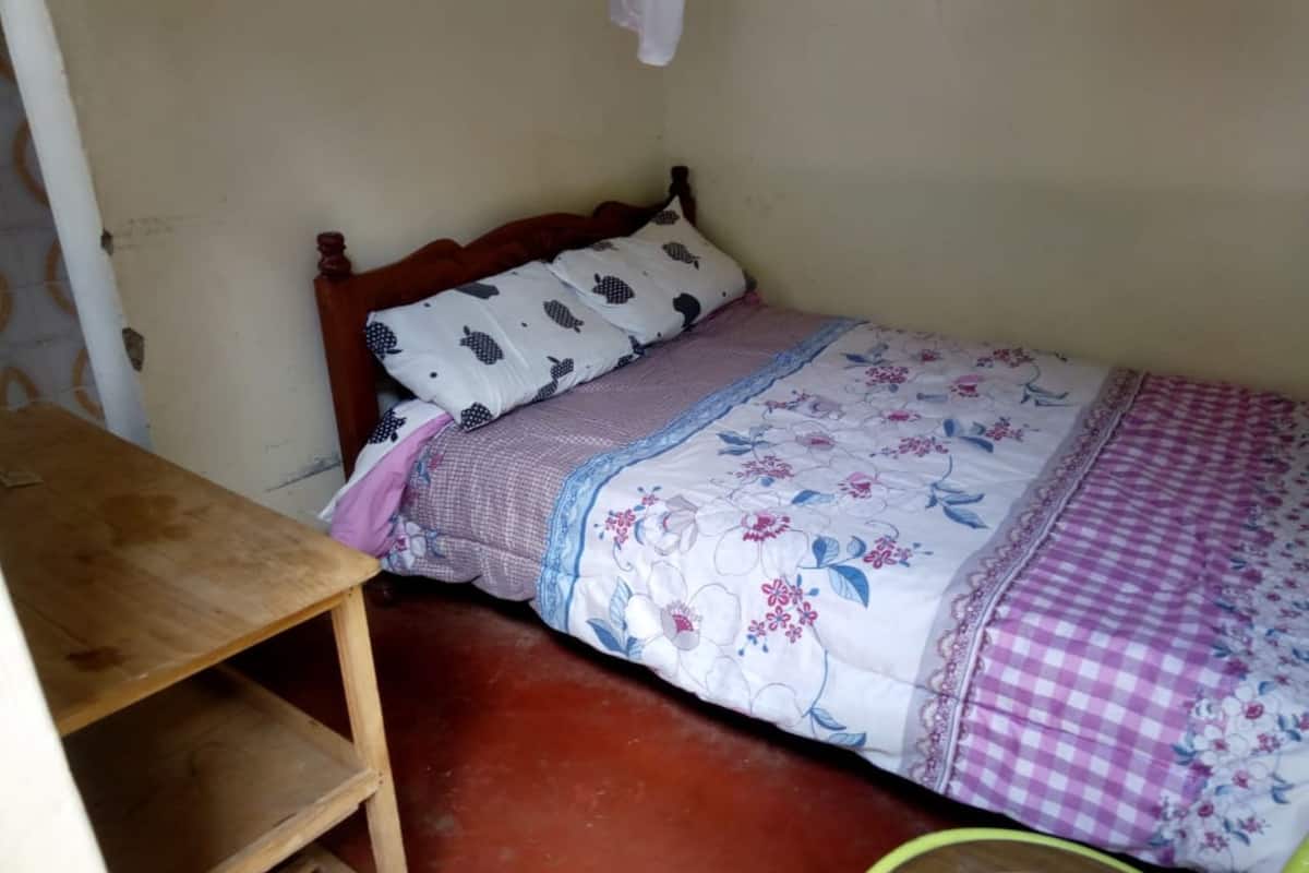 A small, single-bed room with a wooden headboard, a wooden table, and a green chair.