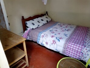 A small, single-bed room with a wooden headboard, a wooden table, and a green chair. - Jostem Inn (Ruiru)