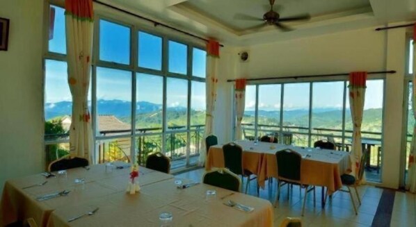A dining area with tables set for guests, large windows offering a mountain view, and a ceiling fan. - Dream World Resort (Ranau)