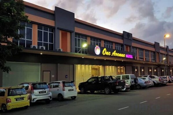 A hotel with a prominent sign, multiple parking spaces, and a clear sky. - One Avenue Hotel (Ijm) (Sandakan)