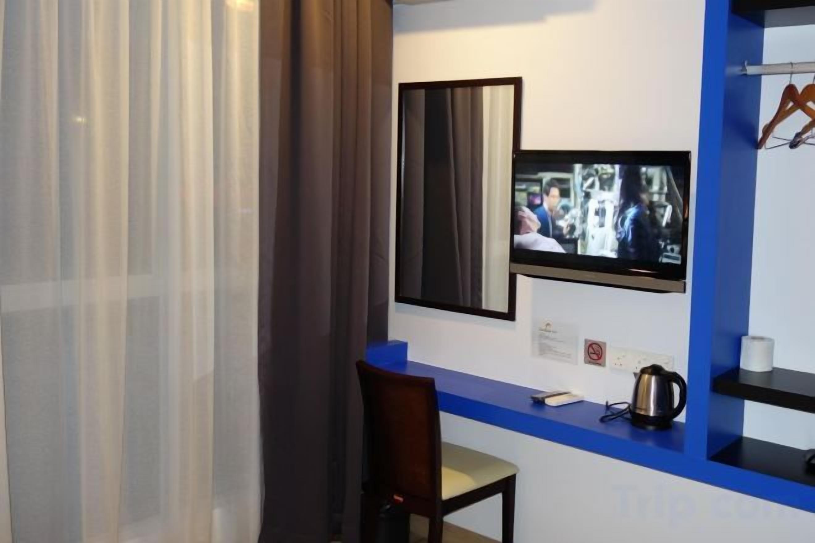 A hotel room with a television mounted on the wall, a desk with a chair, and a coffee maker.