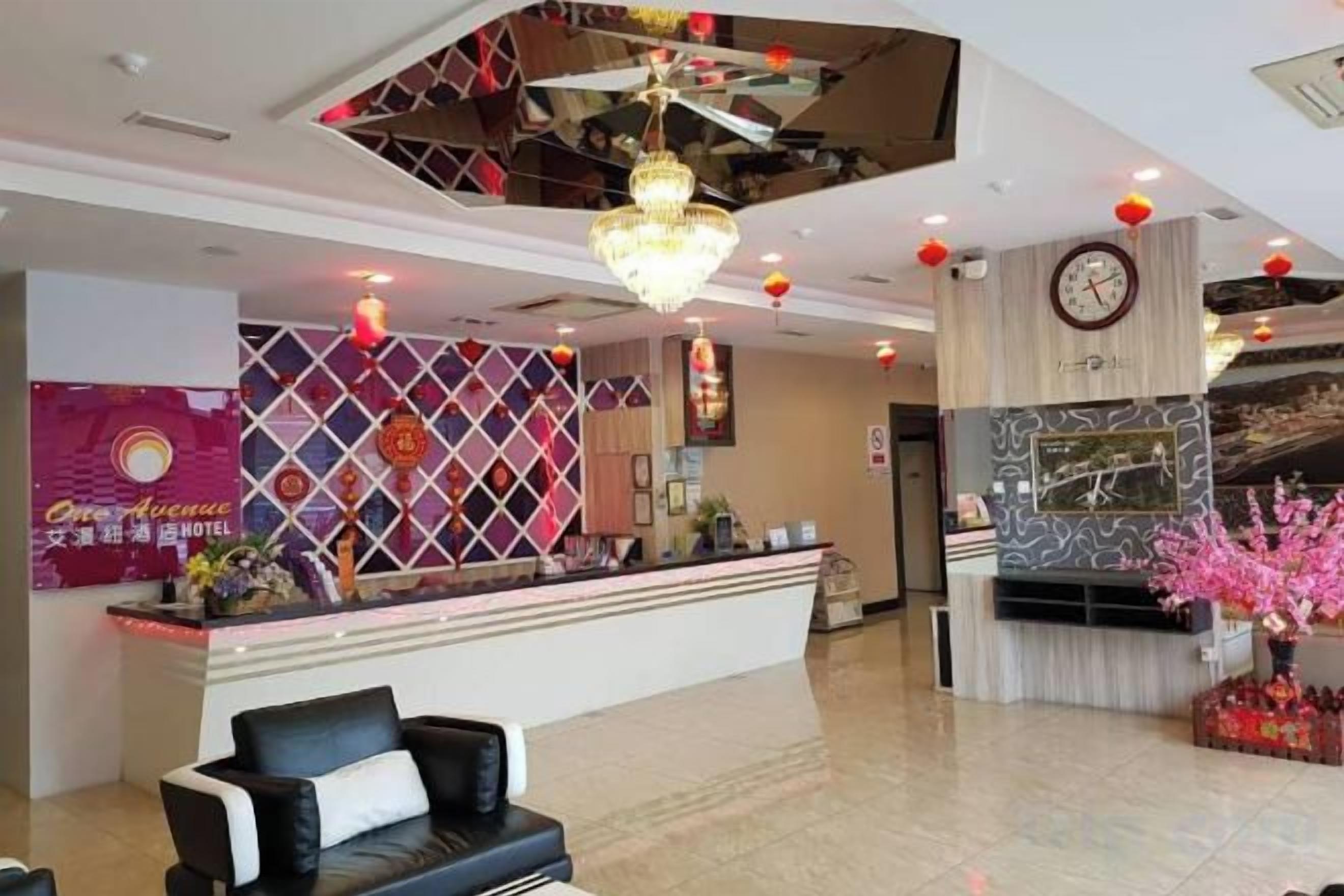 A hotel lobby with a reception desk, a black leather sofa, a chandelier, and a clock on the wall.