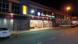 Un hotel llamado 'One Avenue Hotel' con una fachada moderna, grandes ventanales y una entrada visible.