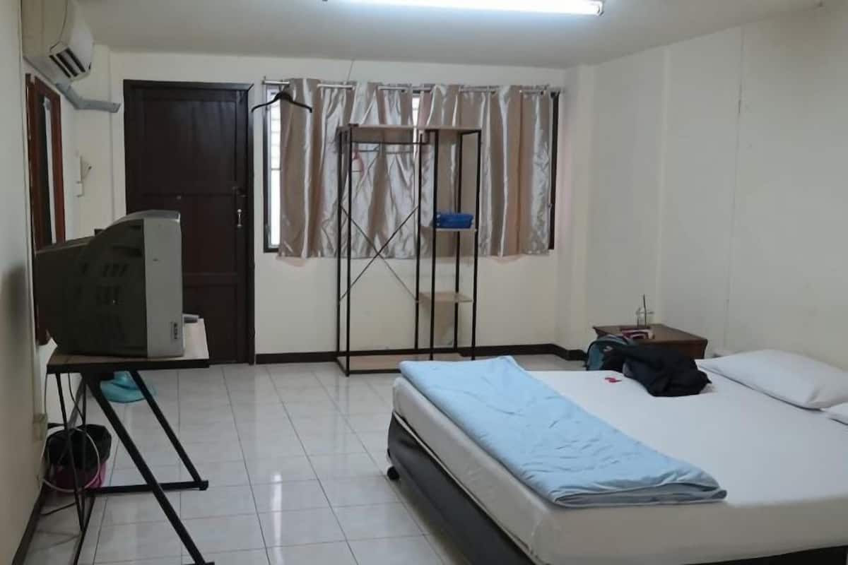 A bedroom with a bed, a television, a wardrobe, a window with curtains, and a small table.