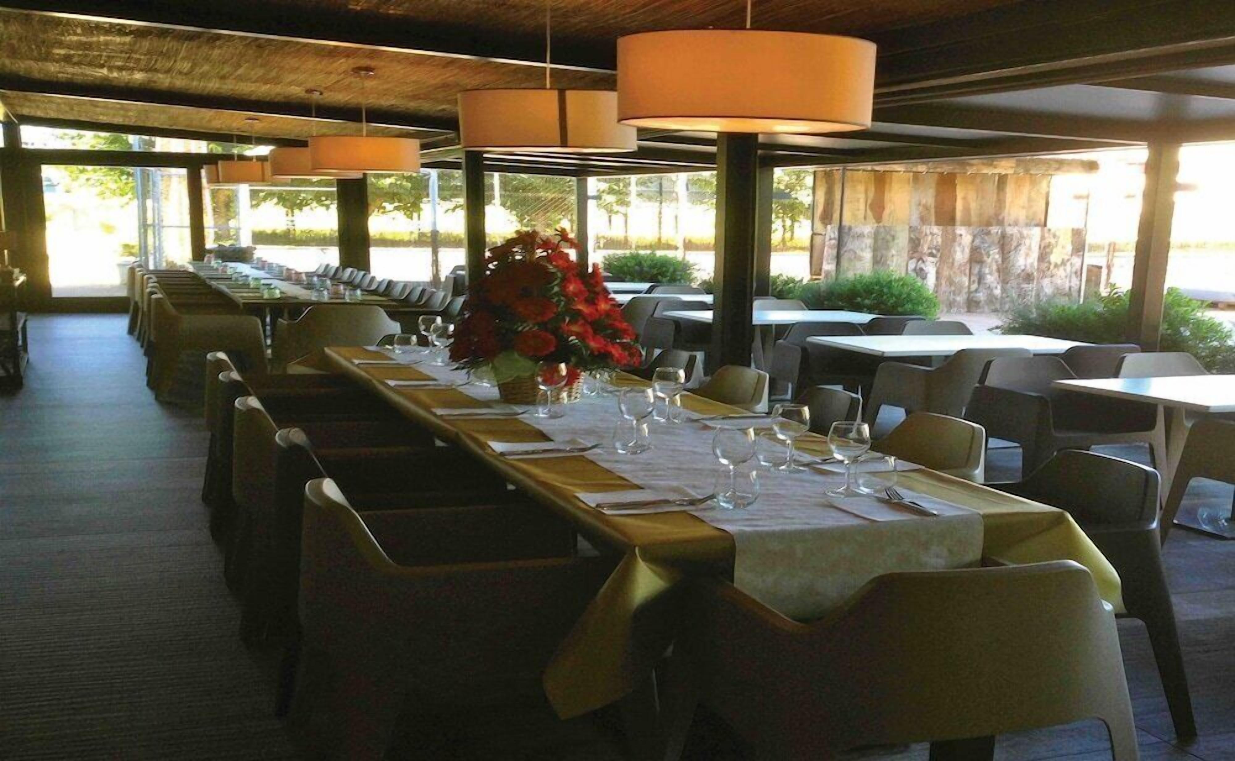 Un restaurante con mesas largas, sillas y lámparas colgantes.