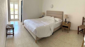 Une chambre à coucher comprenant un lit, des tables de chevet, une chaise et une porte donnant sur un balcon.