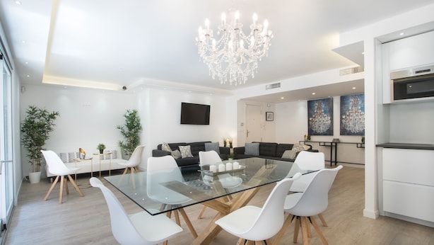 A modern dining area with a glass table, white chairs, a chandelier, and a black sofa. - Large 4BR with AC Steps to the Beach (Alicante (Alacant))