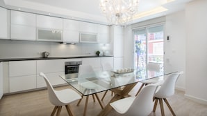A modern kitchen with white cabinetry, a glass dining table, and white chairs. - Large 4BR with AC Steps to the Beach (Alicante (Alacant))