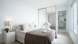 A modern bedroom with a large mirror, a bedside table with a lamp, and a neatly made bed. - Large 4BR with AC Steps to the Beach (Alicante (Alacant))
