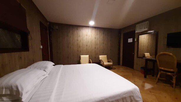A room with a large bed, two chairs, a wooden floor, a ceiling light, and a door. - Dragon Inn Floating Resort (Semporna)