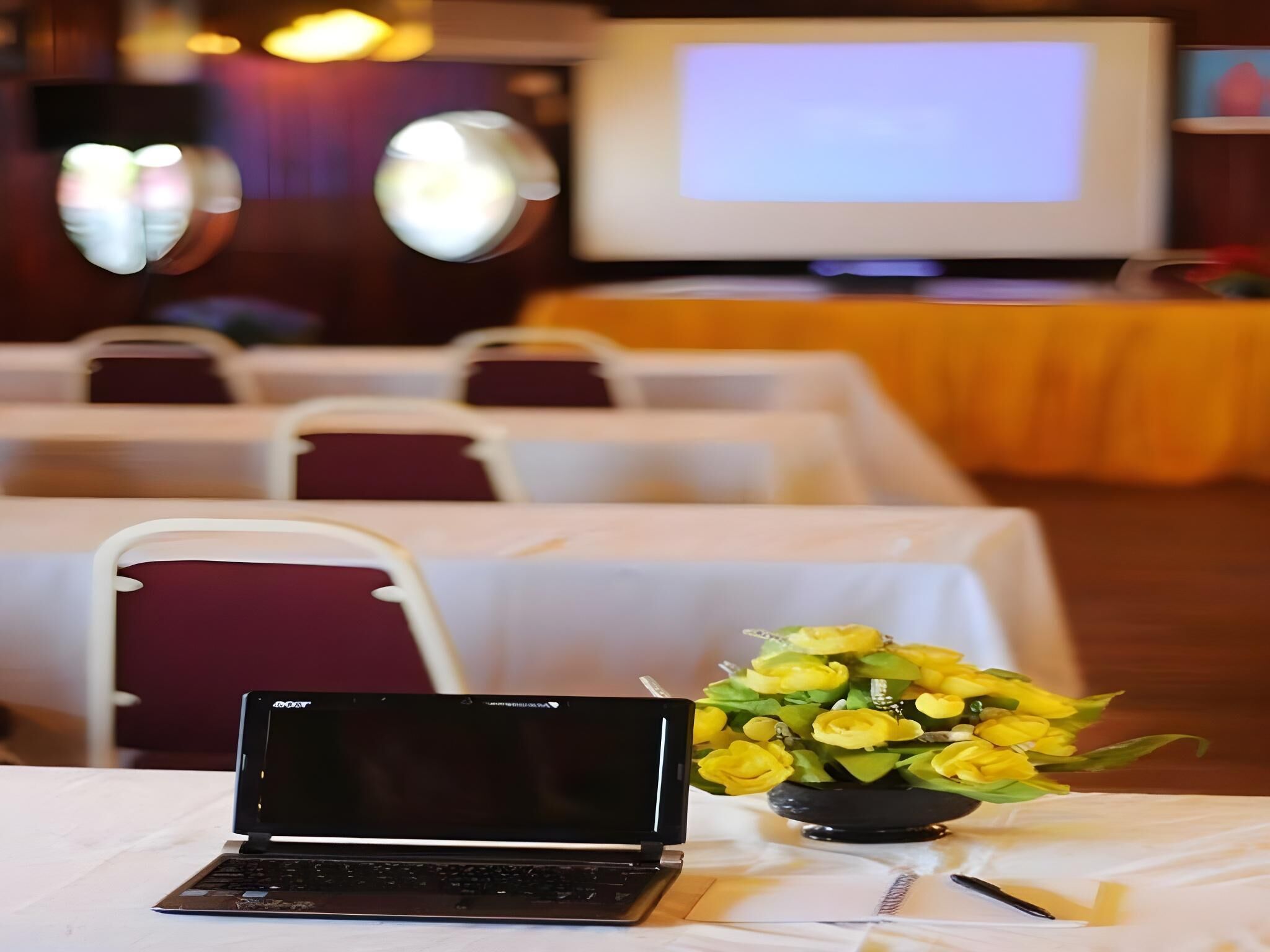 A conference room with tables, chairs, a laptop, and a bouquet of yellow flowers.