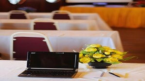 A conference room with tables, chairs, a laptop, and a bouquet of yellow flowers. - Dragon Inn Floating Resort (Semporna)