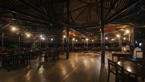 An indoor dining area with wooden tables and chairs, a high ceiling with exposed beams, and ambient lighting. - Dragon Inn Floating Resort (Semporna)