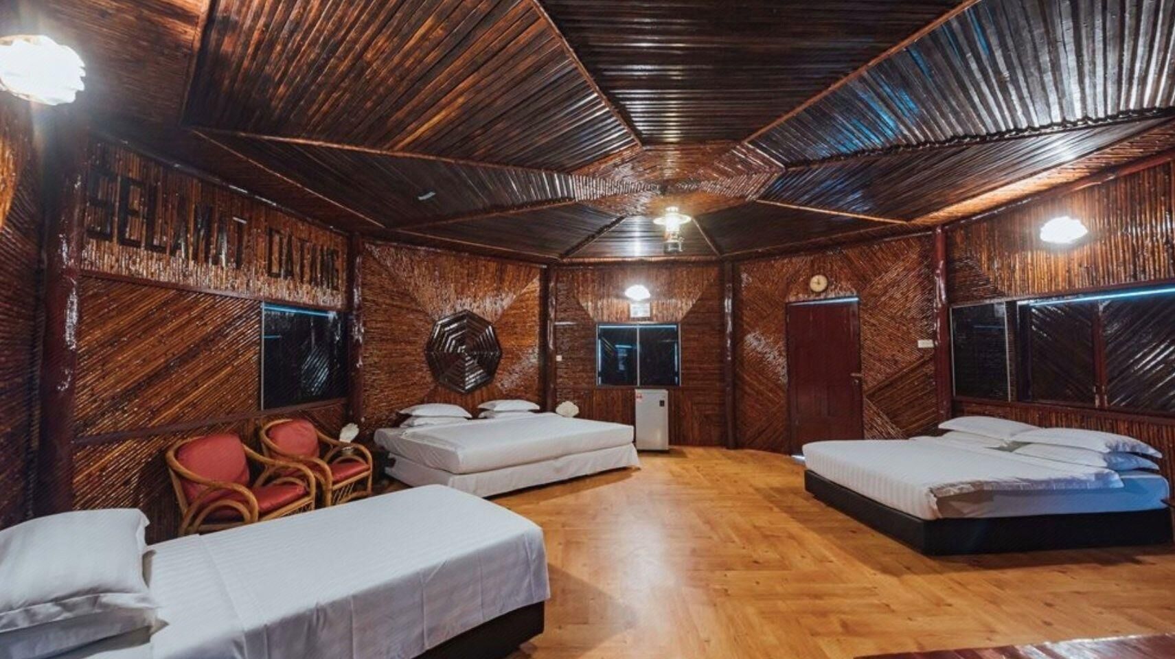A rustic room with wooden walls and floors, three beds, a small table, and a chair.