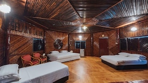 A rustic room with wooden walls and floors, three beds, a small table, and a chair.