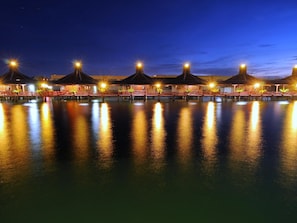 Ein Resort am Wasser mit Bungalows auf Stelzen, die durch Brücken verbunden sind, beleuchtet durch stimmungsvolle Beleuchtung.