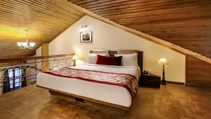 Un dormitorio con techo inclinado, vigas de madera, una cama con almohada roja, dos lámparas de noche y un cuadro enmarcado en la pared.