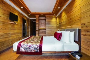 A wooden-paneled room with a bed, a television, and a staircase. - Summit Grace Hotel Spa (Darjeeling)