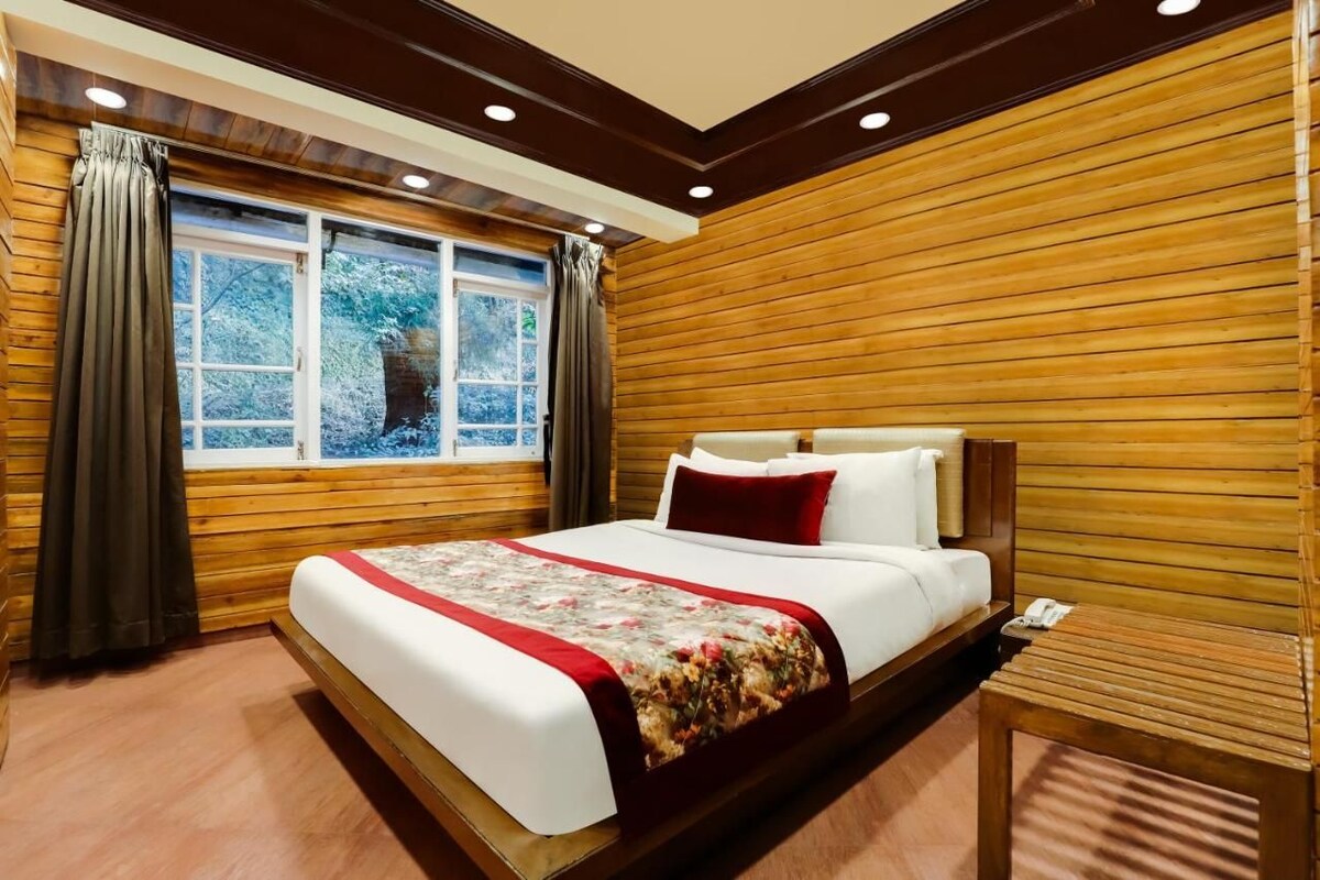 Una habitación con un revestimiento de madera, una cama grande con colcha estampada, una mesita de noche y una ventana con cortinas.