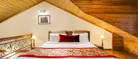 Un dormitorio con techo inclinado, una cama con sábanas blancas y un plaid rojo, dos lámparas de noche y un cuadro enmarcado en la pared.