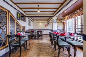 A restaurant with wooden beams, herringbone floor pattern, and tables with red napkins. - Summit Grace Hotel Spa (Darjeeling)