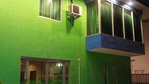 A building with a green exterior, a window with a curtain, and an air conditioning unit. - Green View Motel (Kota Kinabalu)