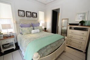 Quarto com cama, mesas de cabeceira, cômoda e espelho.