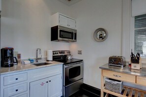 Eine kompakte Küche mit Mikrowelle, Toaster und Kaffeemaschine auf der Arbeitsfläche, einem kleinen Backofen und einem Spülbecken.