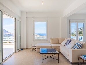 A spacious living room with a sofa, a coffee table, and a view of the sea through large windows. - Villa Mariou south Crete 4 bedrooms (rethymno)