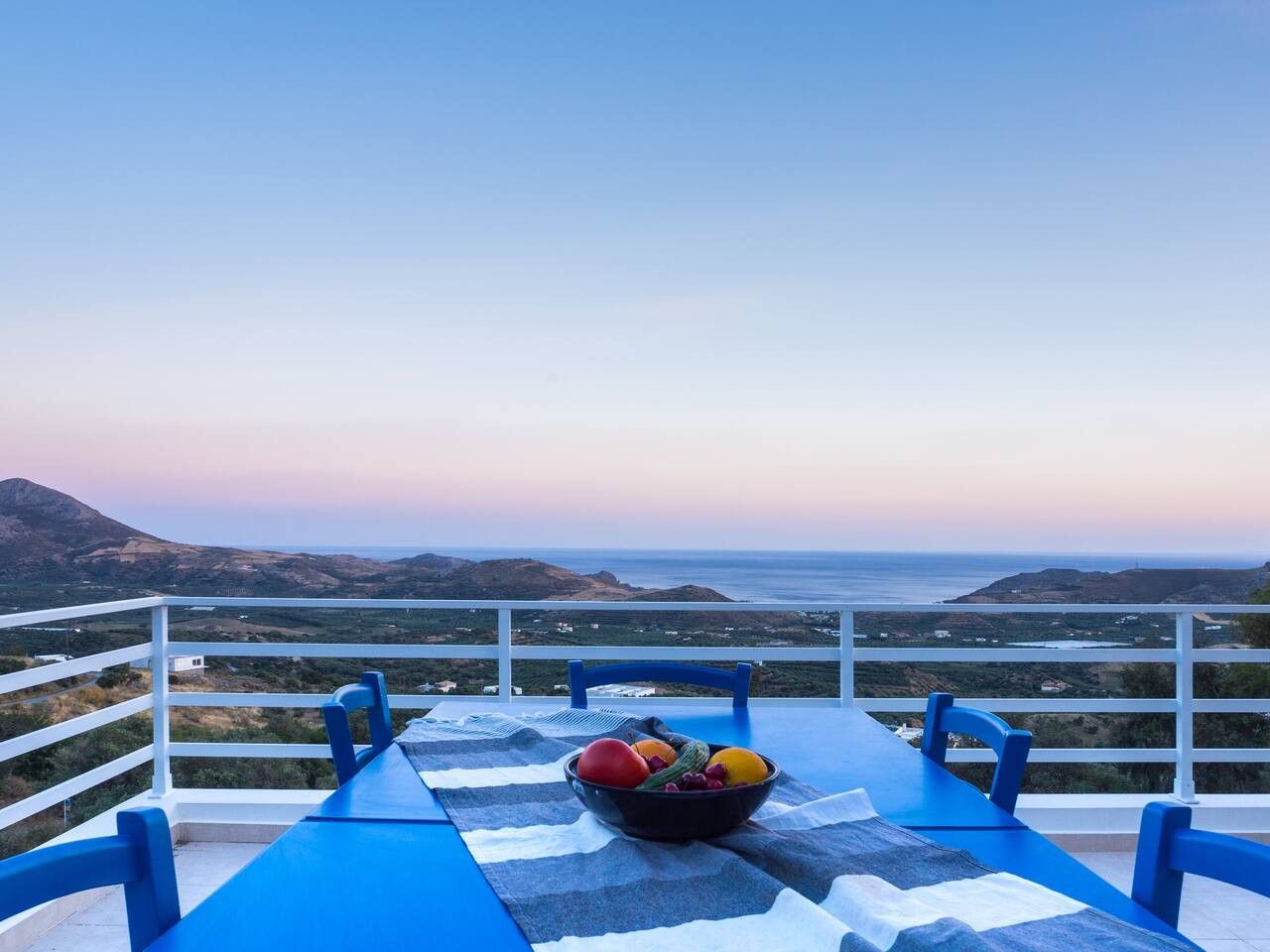 A table with a bowl of fruit and a view of the sea and hills.