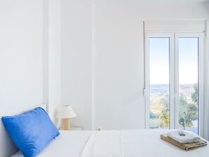 A bedroom with a bed, a blue pillow, a lamp, and a window with a view. - Villa Mariou south Crete 4 bedrooms (rethymno)