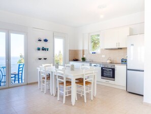 Una cocina moderna con armarios blancos, una mesa de comedor con sillas y vistas a través de puertas de cristal.