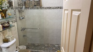 Une salle de bain équipée d’une douche, de toilettes et d’étagères en verre où sont rangés les articles de toilette.