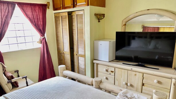 Une chambre à coucher avec un lit, une télévision, une armoire et une fenêtre avec des rideaux.