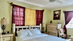 Une chambre à coucher comprenant un lit, des tables de chevet, une commode et un ventilateur de plafond.