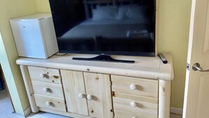 Un téléviseur posé sur un meuble en bois doté de tiroirs, un ventilateur de plafond et une porte visible au fond.