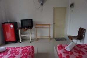 Una habitación con una cama, un escritorio con computadora, un refrigerador rojo, una silla de madera y una puerta.