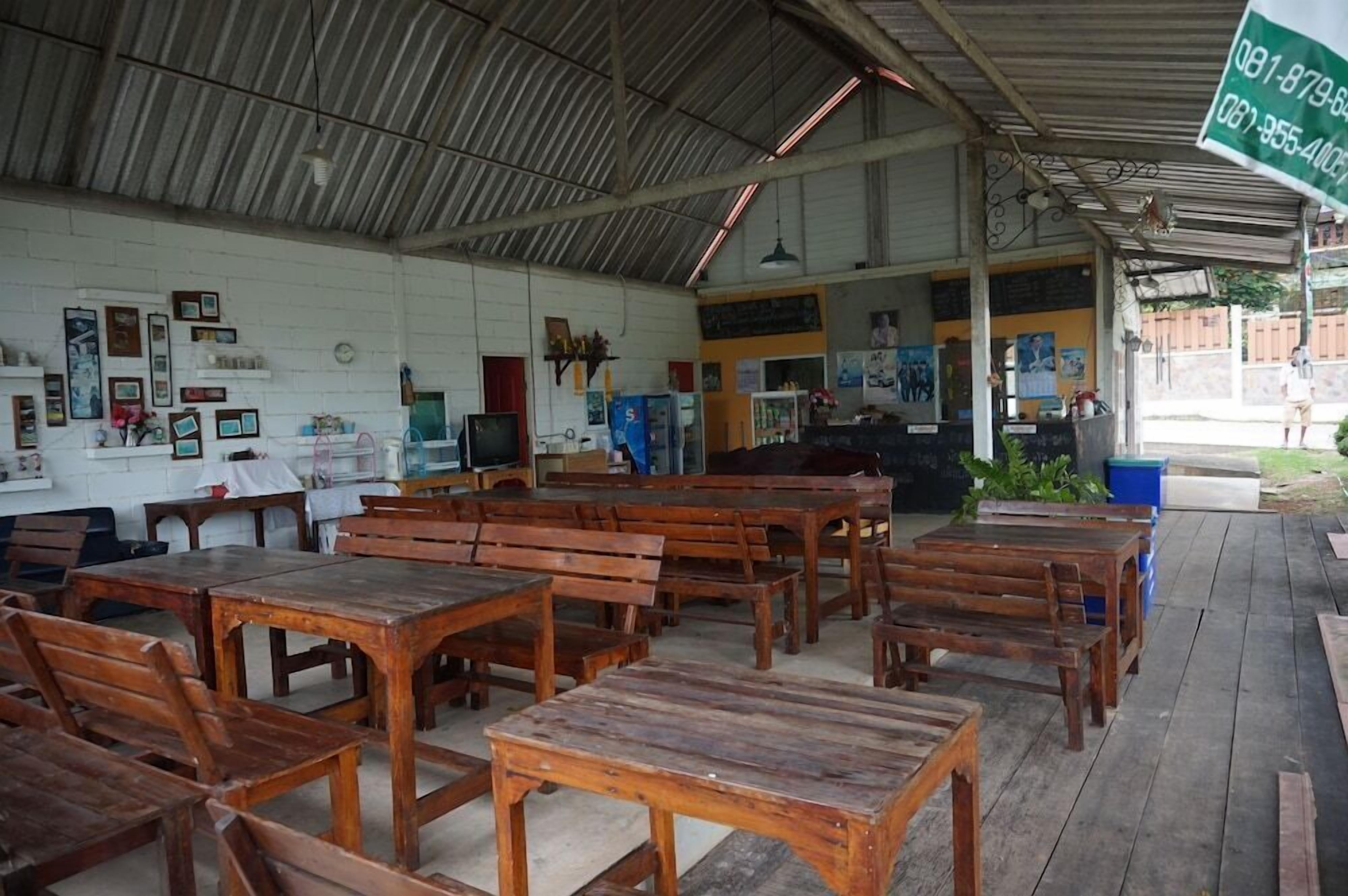 A covered outdoor seating area with wooden tables and benches, a counter with a menu, and a sign with contact numbers.