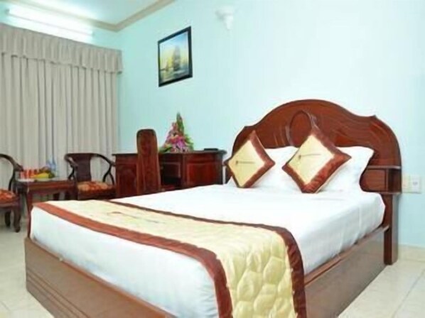 Quarto de hotel com uma cama, uma escrivaninha, uma cadeira e uma janela com cortinas.