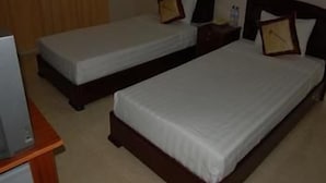 A hotel room with two single beds, a wooden headboard, a nightstand with a lamp, and a television on a stand. - Lam Son Hotel (Vung Tau)