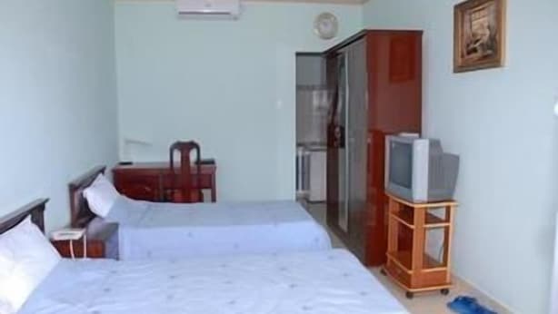 A room with two beds, a television on a stand, a desk, and a door leading to a bathroom. - Lam Son Hotel (Vung Tau)