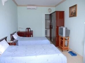 Quarto com duas camas, uma televisão sobre suporte, uma mesa e uma porta que dá para o banheiro.