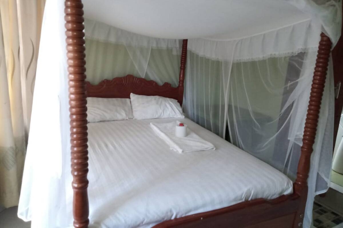 A four-poster bed with a canopy, white linens, and a bedside table with a bottle.