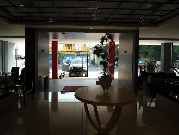 A modern lobby with a glass partition, a round table with a vase, and a view of the street outside.