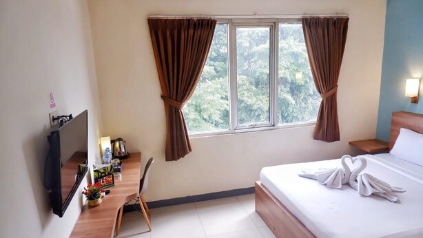 A hotel room with a bed, a desk with a chair, a TV, and a window with curtains. - New Moonlight Hotel (Bandung)