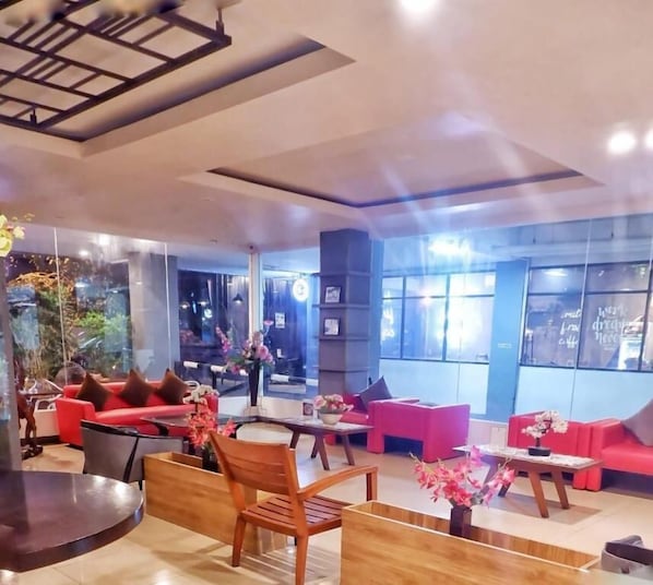A modern interior with red sofas, wooden furniture, and large windows. - New Moonlight Hotel (Bandung)