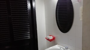 A bathroom with a white sink, a mirror, a red basket, a green trash bin, and a black door. - East & West Dormitory And Guesthouse (Phnom Penh)