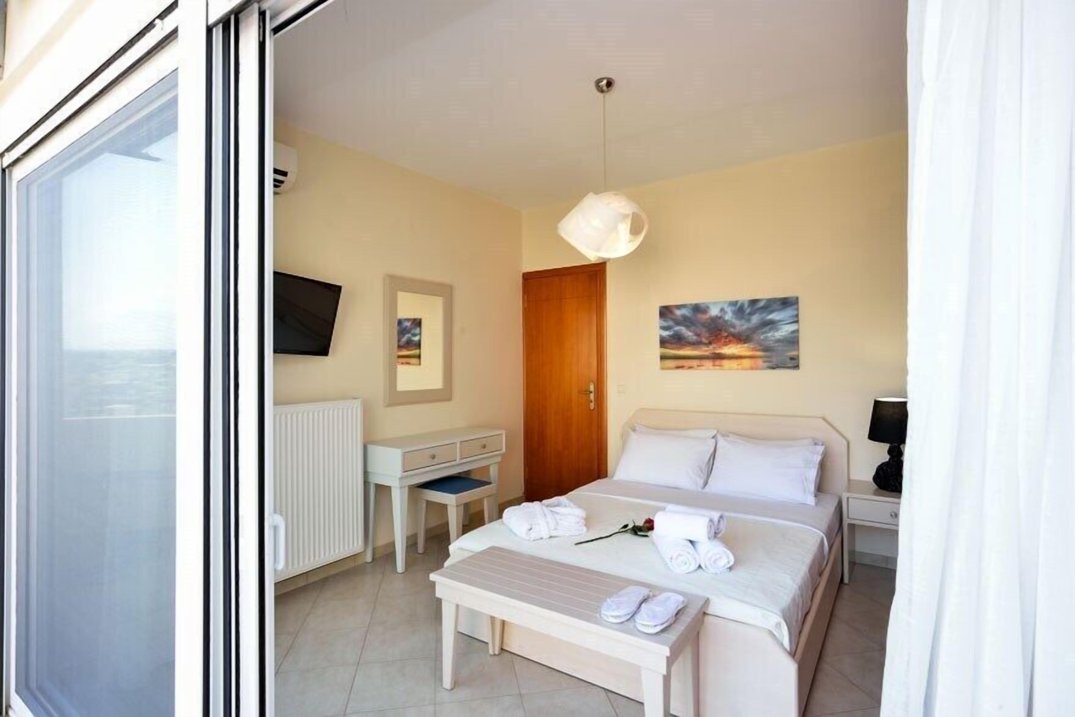 A hotel room with a bed, bedside table, a desk, a chair, a window, and a painting on the wall.