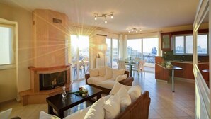 Amplia sala de estar con chimenea, asientos cómodos, zona de comedor y ventanas grandes con vistas a la ciudad.